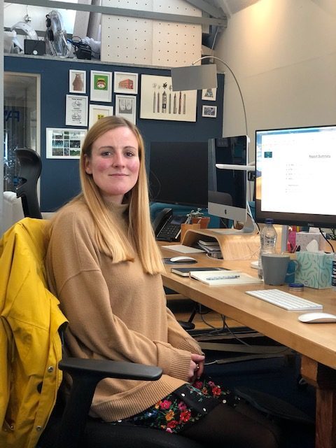 Katie sits at her desk with her face turned towards the camera